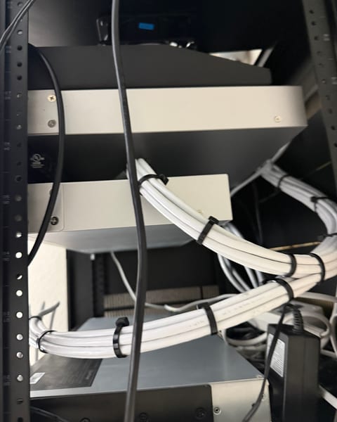 The back of a network rack: bundles of white network cables tied together with black cable ties, running past rack-mounted equipment.